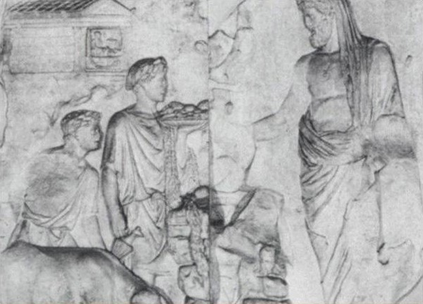 Idomeneo, con il capo velato e l'asta regale, sacrifica la scrofa in onore dei Penati, il cui tempio rettangolare si nota in alto a sinistra (Pannello situato sul lato principale dell'Ara Pacis a Roma)